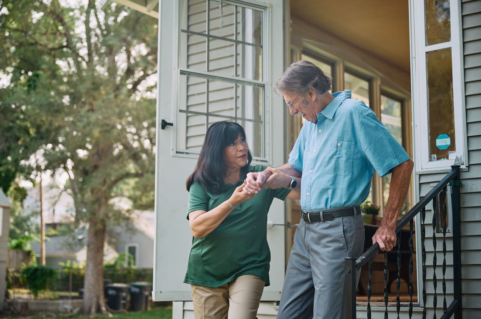A caregiver gently steadying a senior man's hand as he comes down his porch steps