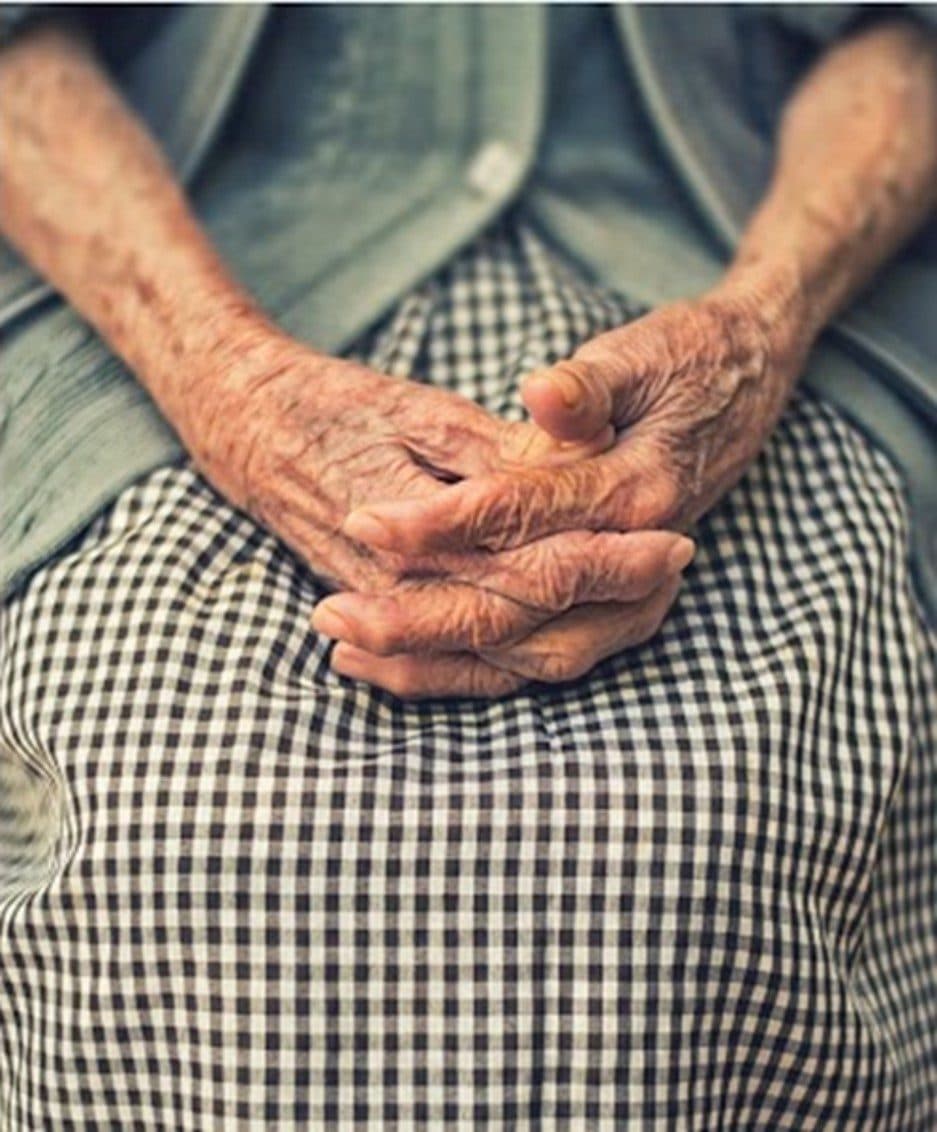 Aged hands gently clasped in a lap, at rest and at ease