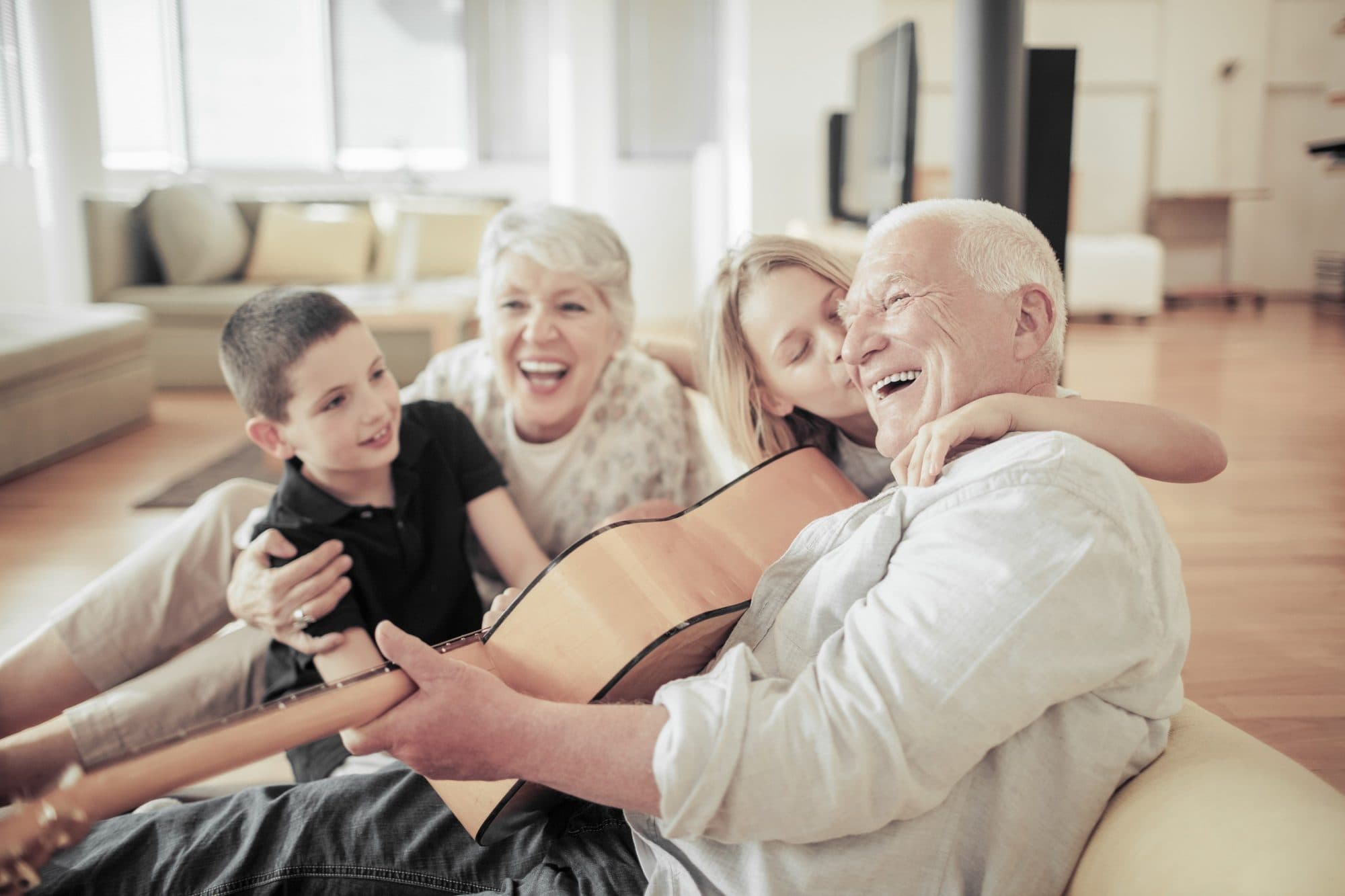 Grandparents laughing with their grandchildren around a guitar at home