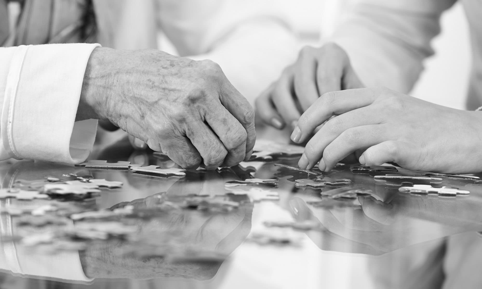 An older adult and a younger helper piecing a puzzle together