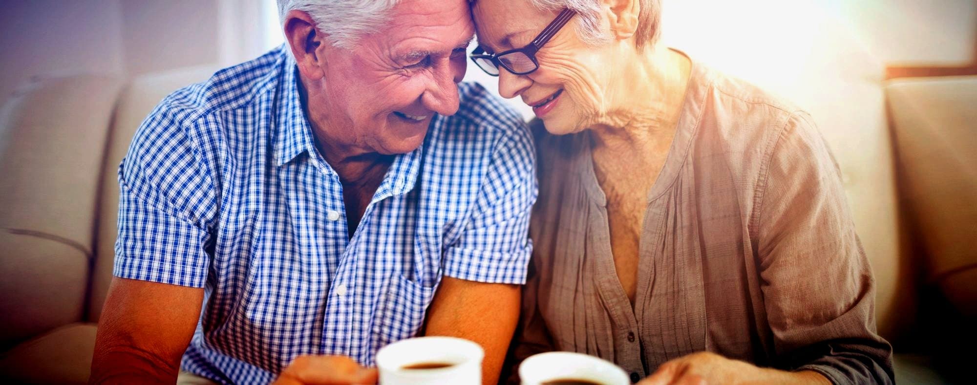 An older couple leaning close together over coffee at home